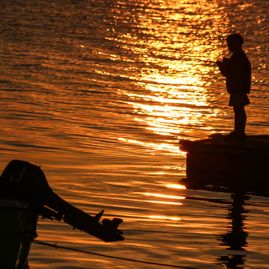 Siluett av gutt på brygge i solnedgang