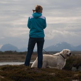 Dame med hund ute på tur i naturen med fjell i bakgrunnen